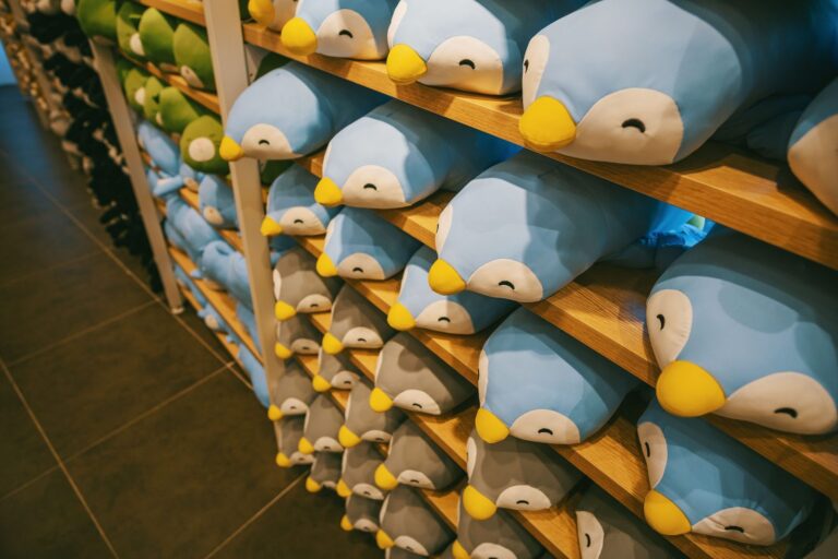 Rows of plush penguin toys stacked on wooden shelves in a toy store